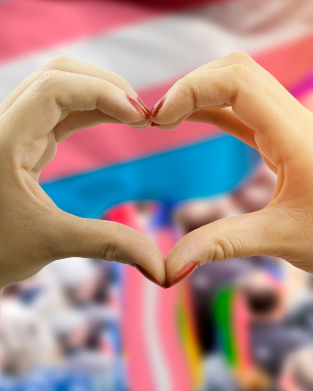two hands in the shape of a heart in front of a crowd and a trans flag flowing