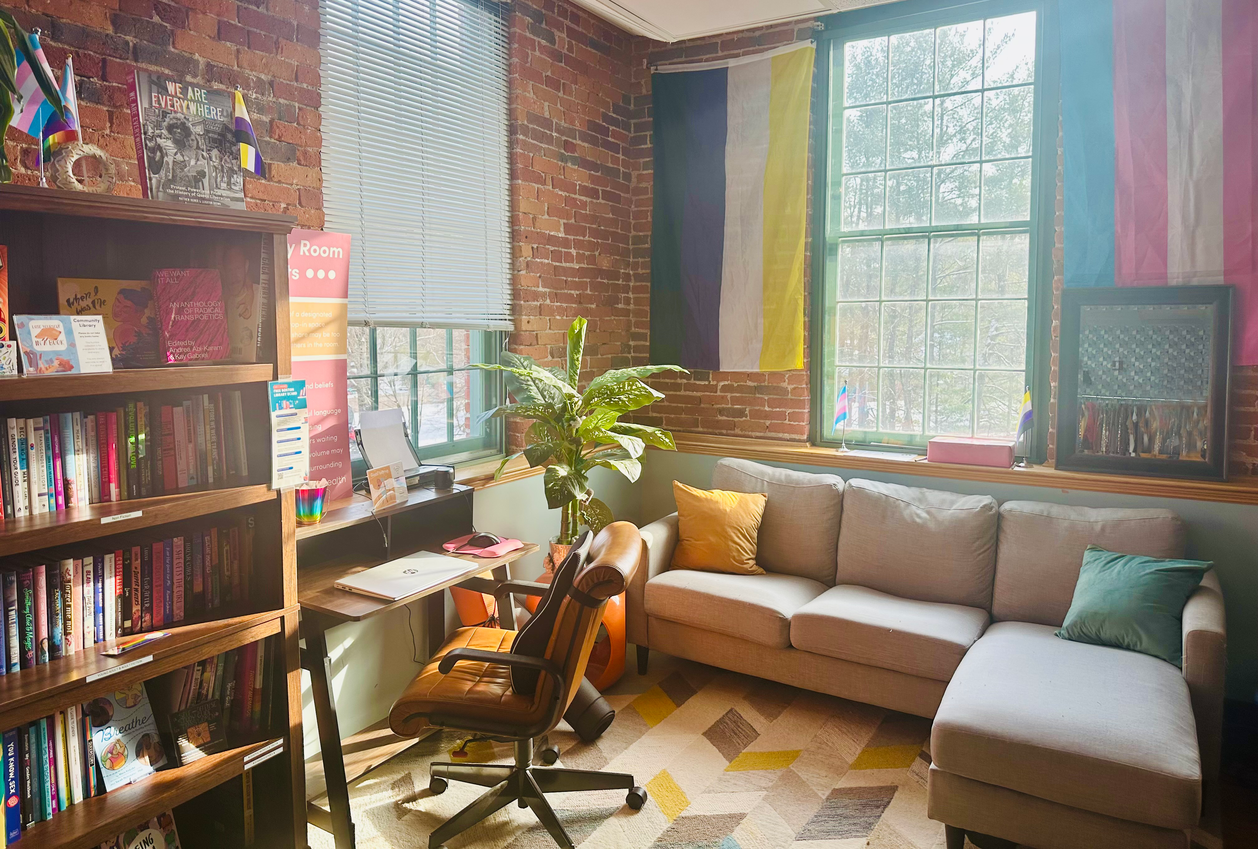 Sun-filled, colorful community room with couch, computer and chair, and book shelves.